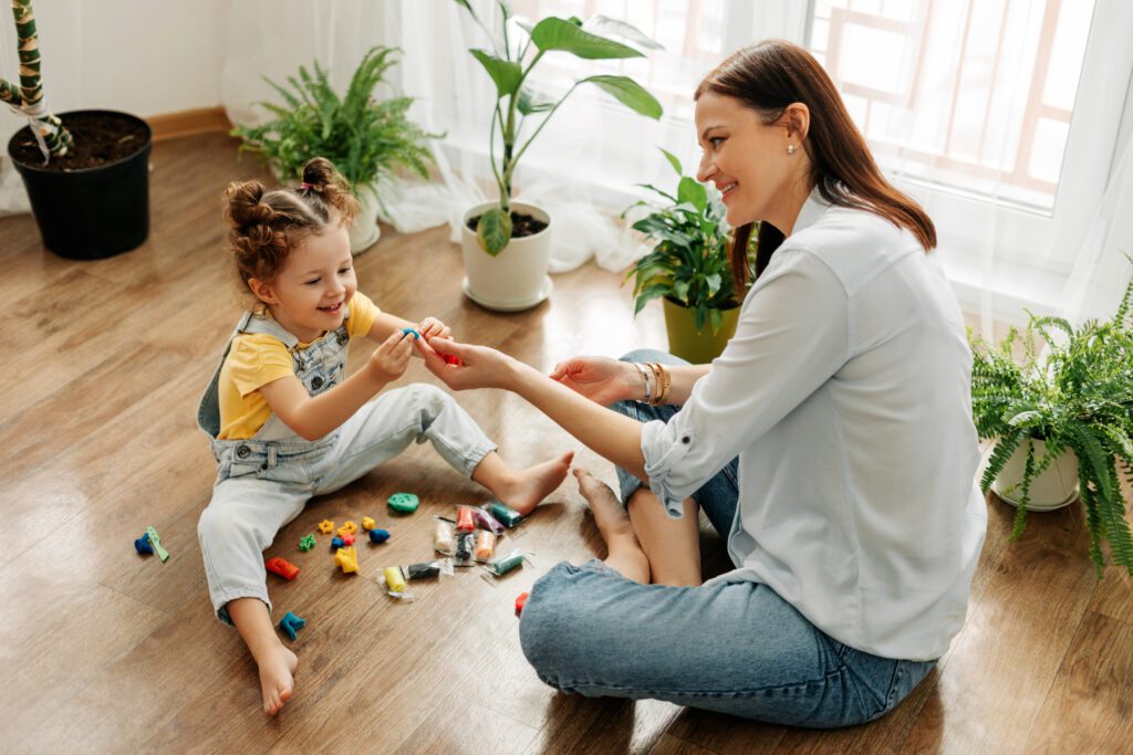 Mom and daughter play together with plasticine at home.